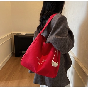 Vista dettagliata della borsa tote in tela rossa con ricamo bianco e ciondolo a tazza
