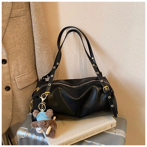 Detail of black leather tote bag with metal eyelets and a cute plush bear pendant