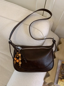 Retro dark brown crescent shoulder bag with wooden bead charm on a woven sofa