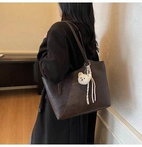 Detailed side view of deep brown tote bag with cute plush bear charm on shoulder