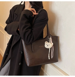 Close-up of brown faux leather tote bag featuring a teddy bear charm and gold logo