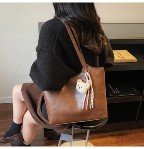 Detail view of large brown leather tote bag with plush bear charm and striped ribbon detail