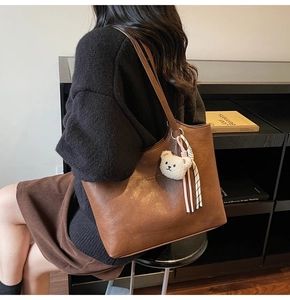 Detail view of large brown faux leather tote bag with a cute white plush bear pendant
