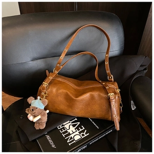 Detail view of brown vintage leather cylinder bag with metal studs and cute bear charm
