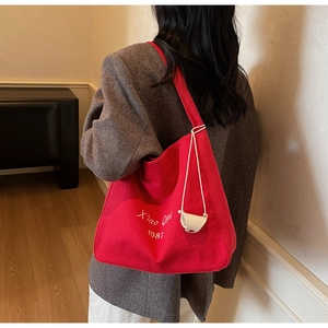Vista dettagliata della borsa tote in tela rossa con tracolla larga e scritte