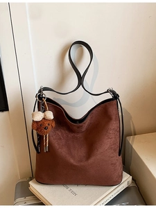 Brown suede tote bag with black straps and bear charm displayed on vintage books