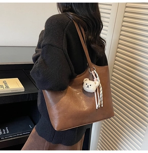 Detail view of large brown leather tote bag with plush bear charm and ribbon