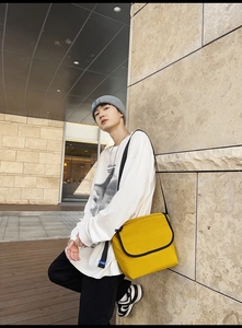 Dettaglio di una borsa a tracolla giallo acceso con bordo nero e chiusura a patta all'aperto