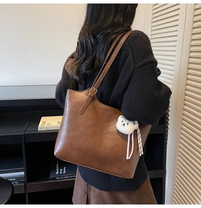 Detail of a brown textured leather tote bag featuring a cute white plush bear charm