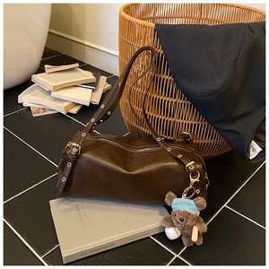 Detail of dark brown cylindrical crossbody bag with gold buckles and cute bear charm