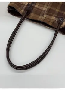 Detail of brown plaid fabric texture and dark leather knotted handle on tote bag