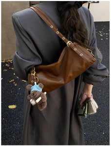 Detail of a vintage brown cylindrical crossbody bag with metal eyelets and a bear charm