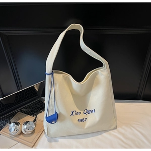 Dettaglio di una borsa tote in tela crema con ricamo blu e mini pochette coordinata