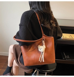 Detailed shot of large brown leather tote bag featuring a cute white teddy bear charm