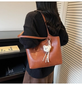 Detail of caramel brown PU leather tote bag with white plush bear charm on strap