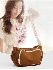 Detailed view of brown travel crossbody bag with contrast white zippers and wide shoulder strap