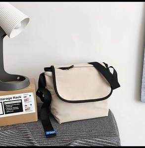 Dettaglio della borsa a tracolla in tela crema con cinturino nero ed etichetta blu