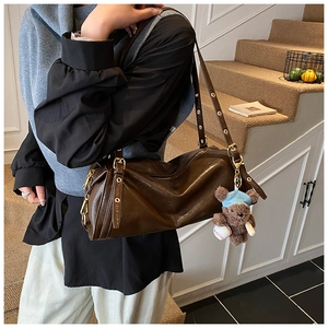 Close-up of dark brown cylinder bag with gold hardware and a cute plush bear charm