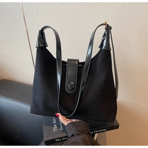 Detail of black suede tote bag with shiny leather trim and decorative round buckle