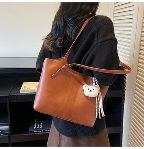 Brown faux leather tote bag detail with white plush bear charm and ribbon accent