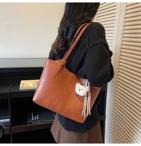 Close-up of brown leather tote bag with plush bear charm and adjustable shoulder strap