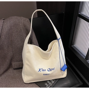 Dettaglio della borsa tote in tela con ricamo blu Xiao Qigai 1987 e mini ciondolo