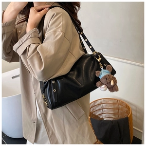 Close-up of black leather shoulder bag with gold hardware and plush bear charm