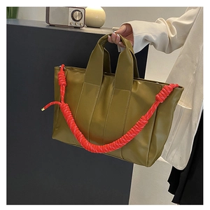 Dettaglio borsa shopper verde oliva con tracolla intrecciata rossa e finitura in pelle PU