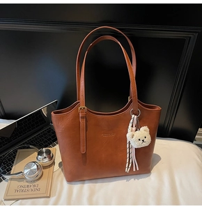 Detail of brown faux leather tote bag with plush bear charm and metallic accents