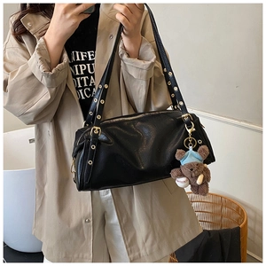 Detail of black cylinder bag showing metal eyelet strap and plush bear charm decoration