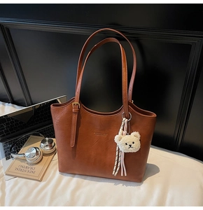 Detail of caramel faux leather tote bag with gold logo, shoulder strap and plush bear charm
