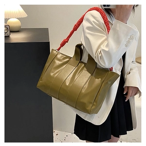 Detail of olive green tote bag with contrasting red pleated long shoulder strap on model