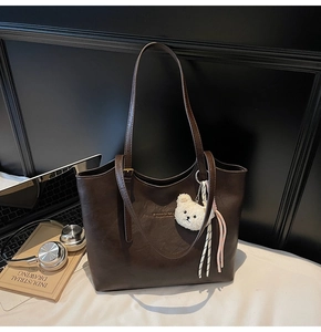Detail of dark brown tote bag with leather texture, golden logo and plush bear charm
