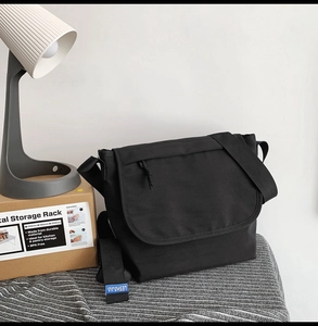 Dettaglio della tracolla della borsa a tracolla in tela nera con etichetta blu di marca