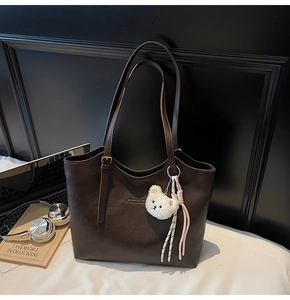 Close-up of dark brown PU leather tote bag with gold logo and plush bear charm