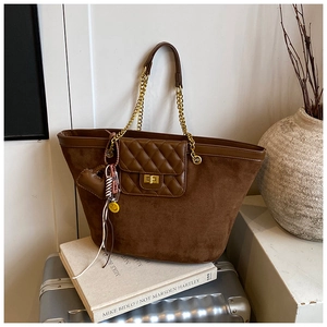 Detail of brown suede tote bag with golden chain strap and decorative heart pendant
