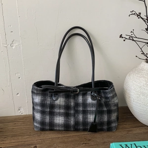 Detail of wool plaid shoulder bag with leather handles on a minimalist wooden setting