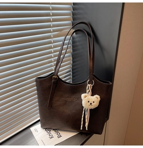 Detail of deep brown faux leather tote bag with gold lettering and cute plush bear charm