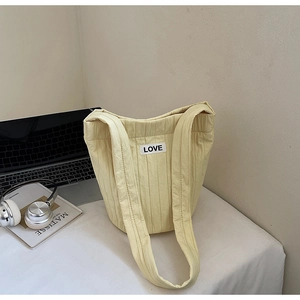 Detail of quilted pale yellow bucket bag featuring a LOVE patch in a minimalist desk setting