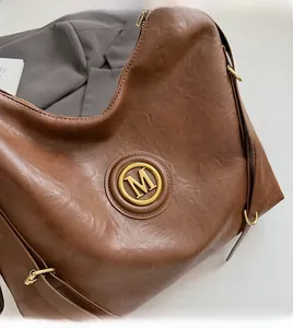 Close-up of brown PU leather shoulder bag featuring a round metal M logo and soft texture