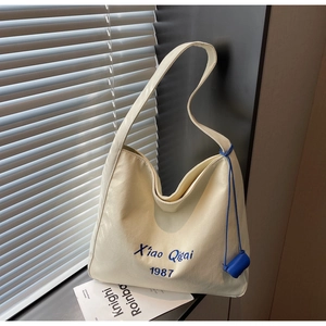 Dettaglio della borsa tote in tela bianca con ricamo blu e cinturino decorativo laterale