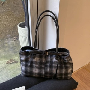 Detail view of plaid tote bag with fine leather buckle and textured wool fabric finish