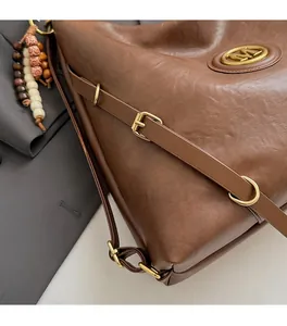 Detailed view of brown leather bag with golden M logo and vintage beaded charm accessory