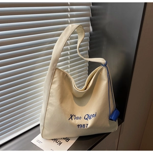 Dettaglio borsa tote in tela color crema con ricamo blu e ciondolo cilindrico blu