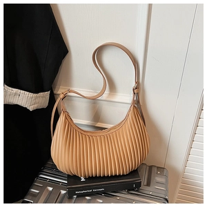 Detail of camel pleated dumpling bag placed on black books against a white wall