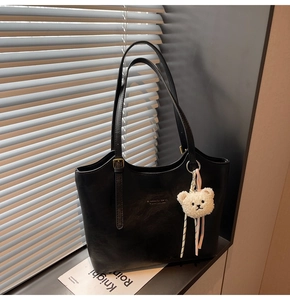 Detail view of black leather tote bag with brand logo and white plush bear charm