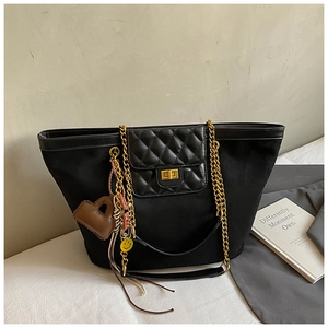 Detail of black tote bag featuring gold chain strap and quilted flap with turn-lock