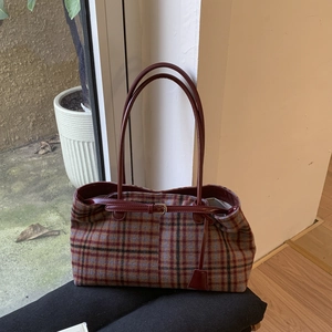 Macro view of vintage plaid tote bag with red leather straps and wool fabric texture
