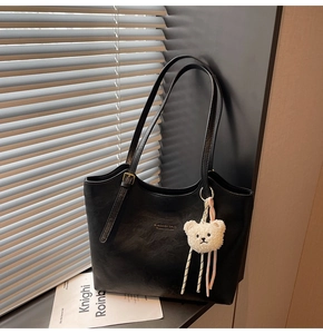 Close-up of black leather tote bag with MIKAXIQI logo and white plush bear charm decor