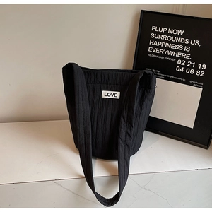 Detail of black pleated tote bag fabric showing the white LOVE patch and soft nylon texture